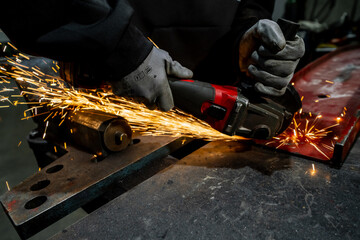 Powertool angle grinder working with metal sparks and hot temperature metal adaption work. Grinding metal with special tools at garage workshop. Red angle grinder held by worker using special gloves