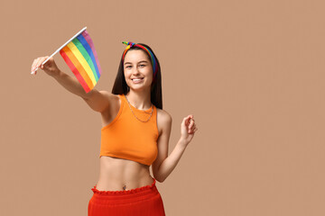 Beautiful young happy woman with piercing navel and LGBT flag on beige background