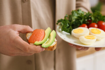 Man holding toast with avocado, salmon, boiled eggs and vegetables, closeup
