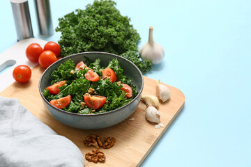 Bowl of tasty kale salad with tomatoes, walnuts and garlic on color background