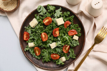 Plate of tasty kale salad with tomatoes, croutons and spices on grey background