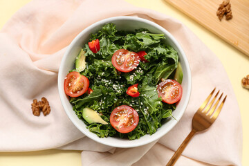 Bowl of tasty kale salad with vegetables, sesame seeds and napkin on color background