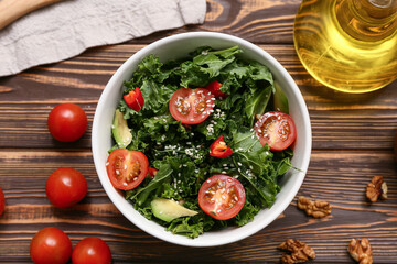 Bowl of tasty kale salad with vegetables, walnuts and oil on wooden background