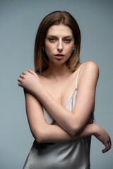 Elegant woman in a silver satin dress posing stylishly. Accessories include sunglasses and a plaid blazer. Modern, sophisticated, and minimalistic fashion. Neutral background enhances the chic aesthet