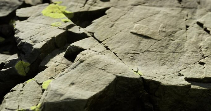 At a close look, the rock surface reveals detailed textures and cracks, interspersed with hints of bright green moss. This natural setting highlights geological diversity and beauty.