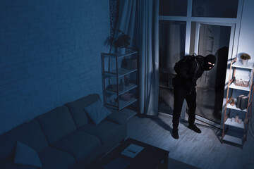 Life After Lockdown. Disguised stealthy robber entering apartment in the dark, holding crowbar,...