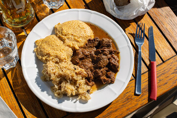 Trentino-Alto Adige traditional mountain cuisine, North Italy. Slowly cooked Venison or deer meat with onion and tomato sauce, served with polenta and sauerkraut, Top view.