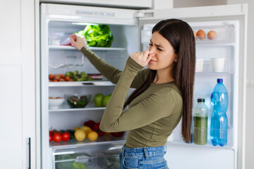 Lady holding nose cause of bad smell from refrigerator in kitchen, opening fridge, searching...