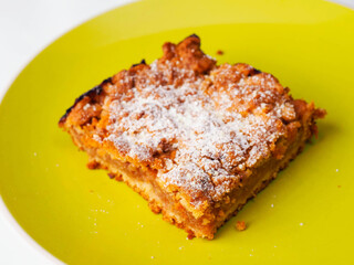 A yellow plate with a piece of cake on it. The cake is covered in powdered sugar. The plate is placed on a white background. Premium slice of a fine bakery product