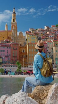 Beautiful woman in a hat stands in the background colorful houses in Menton, France. Cote d'Azur, France