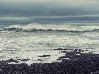 The ocean is rough and the sky is cloudy. The waves are crashing against the rocks. Scene is tense...