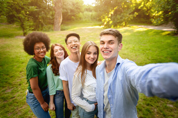 Group of multiethnical teen friends talking selfie outdoors in park, posing for photo together, smiling at camera, free space