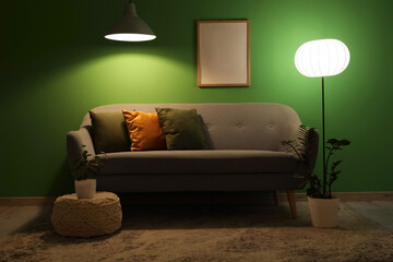 Interior of living room with sofa, blank frame and glowing lamps in evening