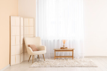 Armchair with folding screen and table near light curtain in room
