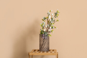 Vase with tree branches and Easter eggs on shelf near beige wall © Pixel-Shot