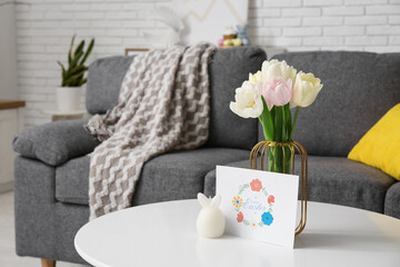 Vase with tulips and card for Easter on table in living room, closeup