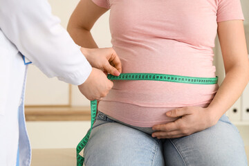 Female doctor measuring pregnant woman's belly in clinic, closeup