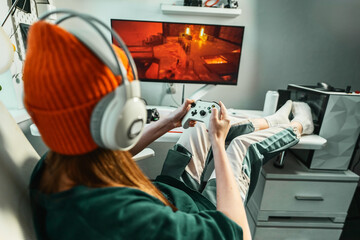Gamer girl with professional headphones relaxing in gaming room playing shooter video game on...