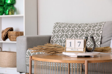 Cube calendar with date of St. Patrick's Day, horseshoe and spikelets on table in living room