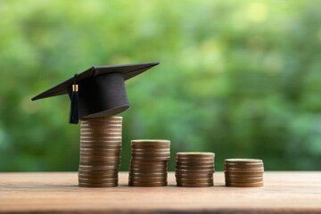 Stacks of coins with graduation hat on table near green blackboard, closeup. Student loan concept 

