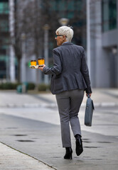 Professional woman walking with coffee and briefcase in city