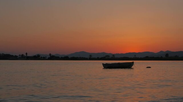 Fish boat in the middle of dusk lake. A view of alone empty fishing boat on lake against bright sky in evening.