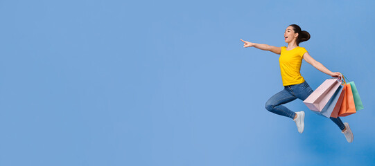 Big Sales. Excited Asian Girl Running With Shopping Bags And Pointing At Copy Space Over Purple Background, Full-Length Portrait In Motion, Side View