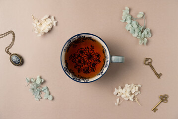 Cup of tea with vintage medallion, keys and flowers on beige background from above. Flat lay, top view.
