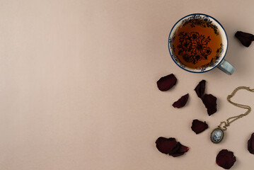 Cup of tea with vintage medallion and rose petals on beige background from above. Flat lay, top view. Copy space