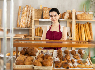 Young woman seller in apron at counter with pastries in bakery