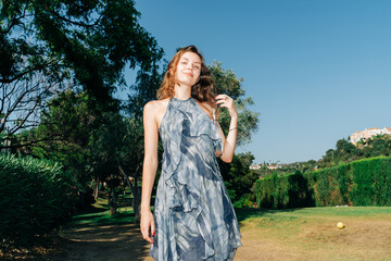 Young caucasian female in blue dress enjoying sunny day in park