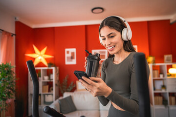 woman exercise on elliptical machine and use mobile phone at home