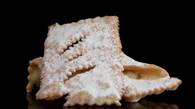 A 360-degree view of crispy Dolci di Carnevale called chiacchiere, dusted with powdered sugar, rotating on a black background. Traditional Italian carnival sweets, perfect for food content.