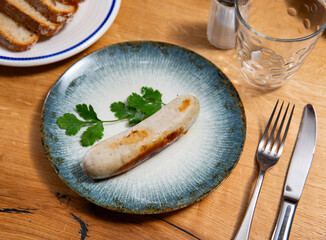Cooked roasted homemade sausage ready for eat. Homemade sausage is made from several varieties of selected meat and using olive oil, spices and fresh herbs. Wooden table, checkered tablecloth, cutlery