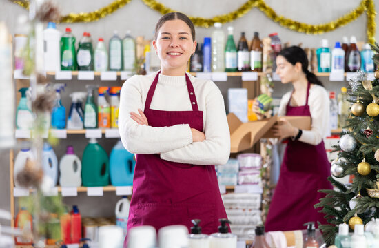 Woman seller invites to shop at Christmas discounts, standing in the household department of a supermarket. Saleswoman offers to get acquainted with the products and promotions for the New year