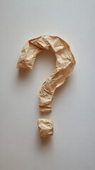 Obraz premium Crumpled brown recycled paper forming question mark against white surface, symbolizing uncertainty and thoughtful inquiry