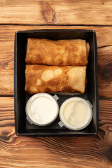 Delicious golden pancakes with creamy dipping sauces served in a black takeout box on a rustic wooden table