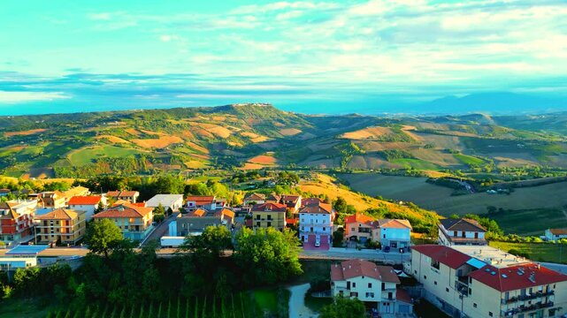 Sumptuous aerial pedestal up shot from Montefiore dell'Aso (AP), soaring to encompass the gently woven, checkered Marche hillscapes of green and brown, with buildings, road and cars in the foreground