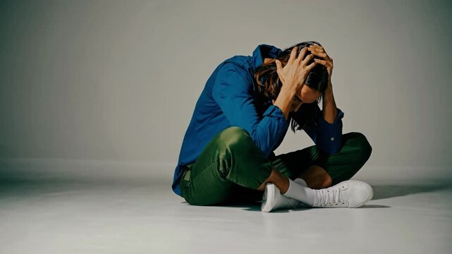 A dramatic video scene shows a person sitting on the floor, head in hands, captured from a low angle, emphasizing emotion and introspection.