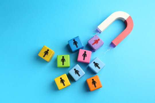 Magnet attracting colorful cubes with human figures on light blue background, top view. Recruitment or customer acquisition