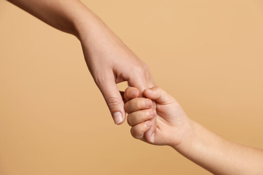 Mother and child holding hands on beige background, closeup