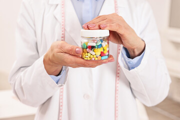Nutritionist with bottle of weight loss pills in clinic, closeup