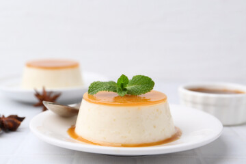 Tasty pudding with caramel sauce served on white tiled table, closeup