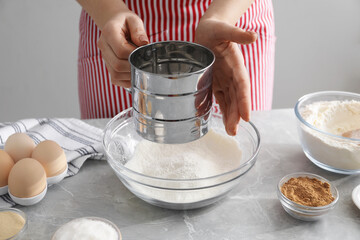 Making cinnamon rolls. Woman sieving flour at gray marble table, closeup