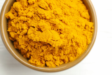 Turmeric powder in bowl on white wooden table, closeup. Top view
