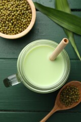 Fresh mung bean juice in mason jar, seeds and leaves on green wooden table, flat lay