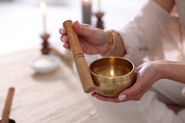 Woman with singing bowl and burning candles indoors, closeup