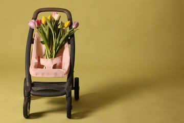 Stylish doll stroller and tulips on olive background, space for text. Kid's toy