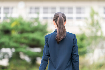 学校の校舎の前に立つ制服姿の中学生・高校生・小学生の後ろ姿

