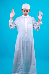 Young Asian Muslim Boy Raising Hands Doing Takbir Praying Salah On Blue Background